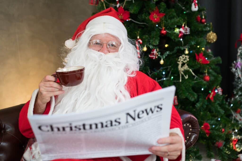 Senior man in Santa Claus costume reading newspaper and drinking coffee