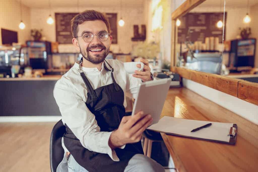 Joyful man drinking coffee and using tablet computer in cafe