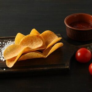 Potato chips on a wooden board with salt on a dark background